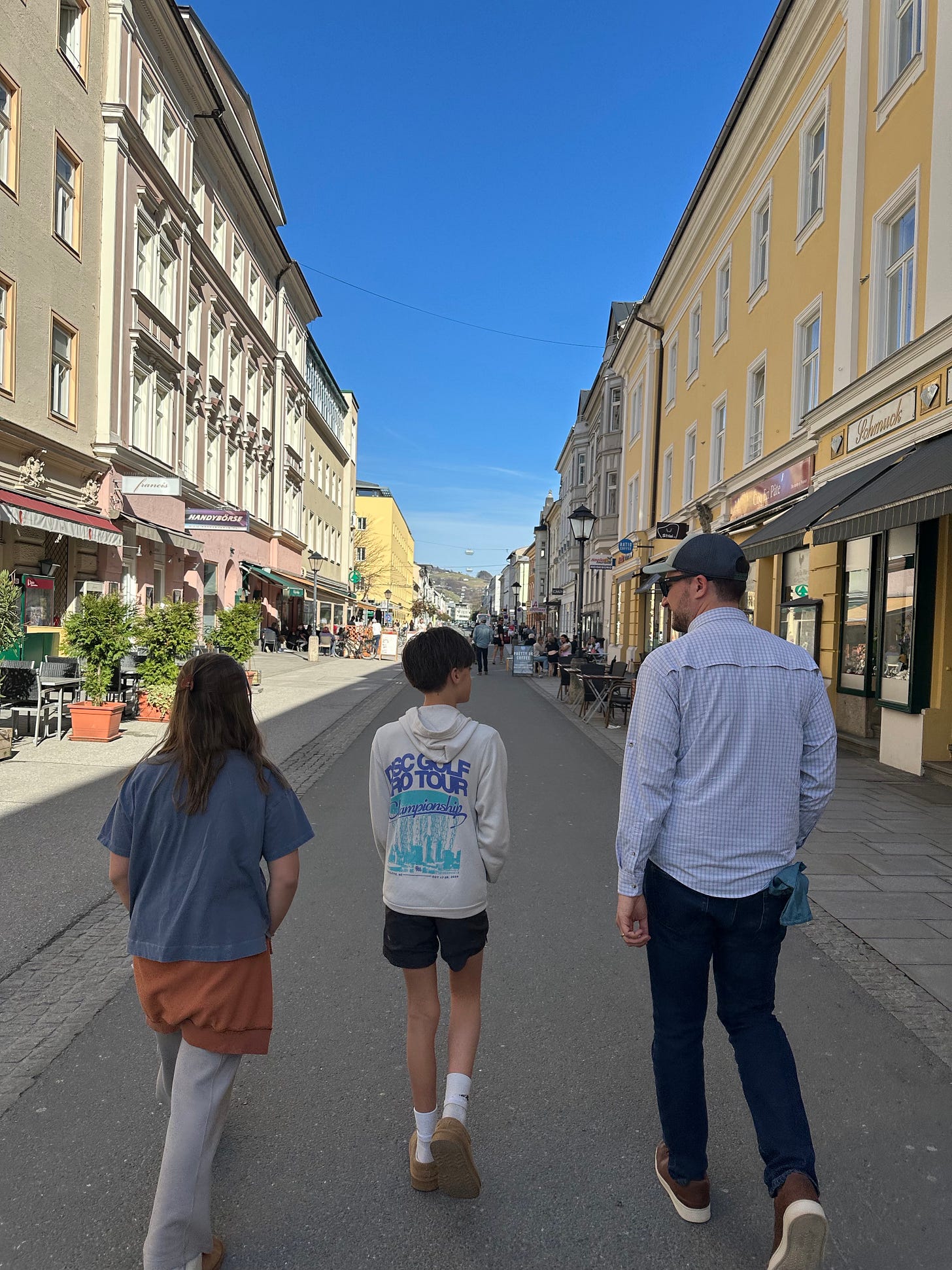 Three people walking down a sunny street lined with colorful buildings and shops.