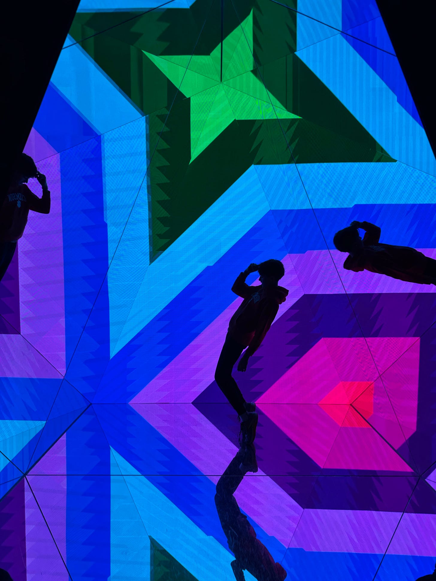 A colorful digital display featuring geometric patterns in blue, green, and pink shades, with silhouettes of two people posing against the vibrant background.