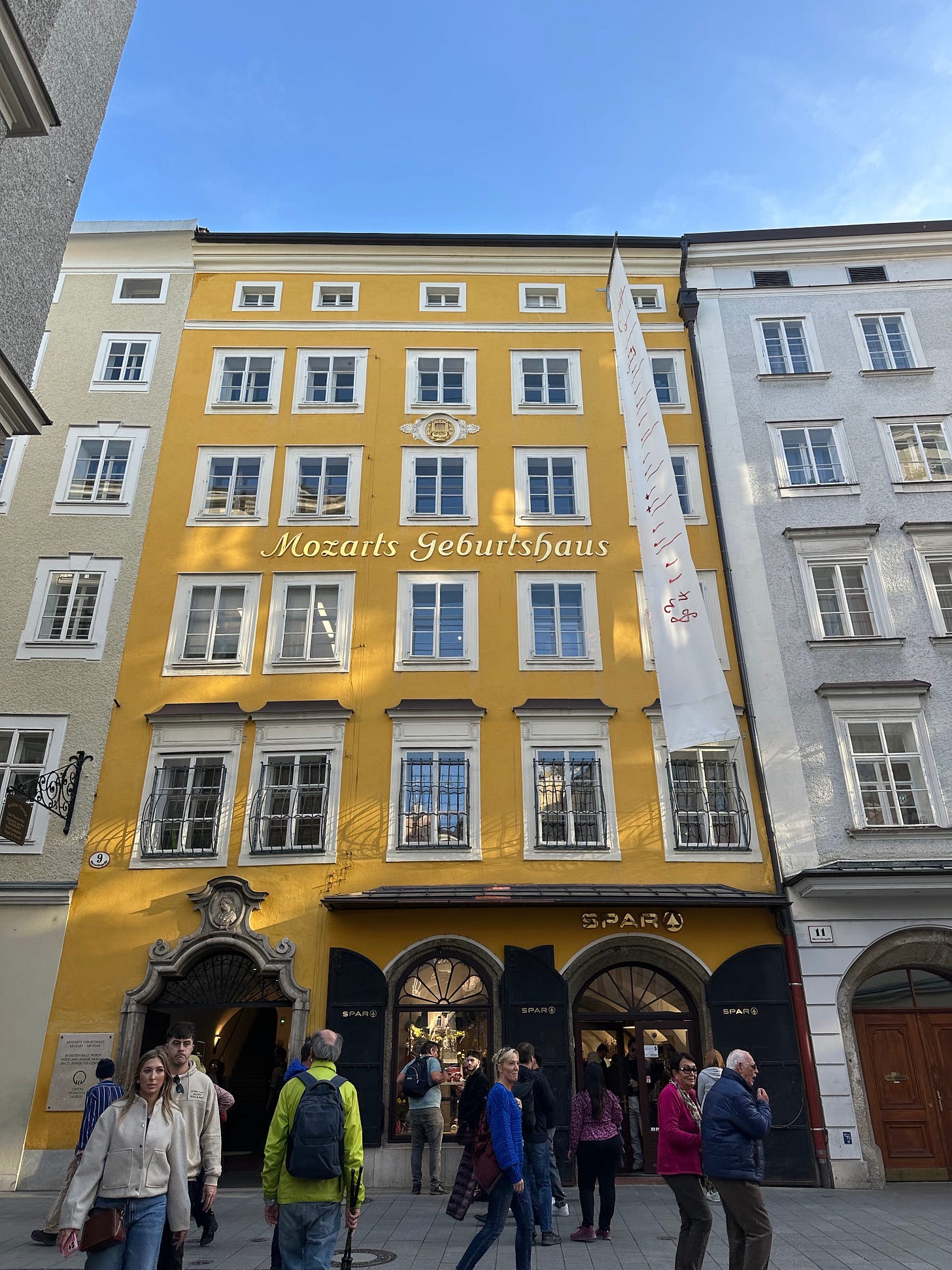 Mozart's birthplace, a yellow historic building with the inscription 'Mozarts Geburtshaus', surrounded by pedestrians in a lively street.